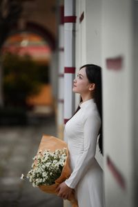 Elegant Vietnamese student in white Ao Dai reading, timeless beauty amidst classic architecture.-0
