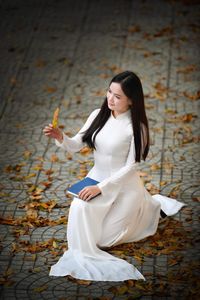 Elegant Vietnamese student in white Ao Dai reading, timeless beauty amidst classic architecture.-15