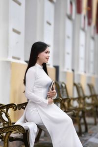 Elegant Vietnamese student in white Ao Dai reading, timeless beauty amidst classic architecture.-9
