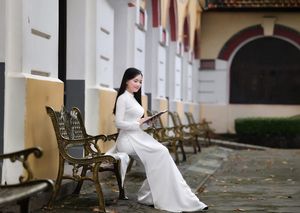 Elegant Vietnamese student in white Ao Dai reading, timeless beauty amidst classic architecture.-6