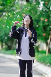 Radiant Youth: Girl in Uniform Playfully Blowing Bubbles in Lush Greenery 1000019736-0