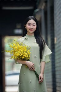 Graceful Vietnamese girl in green Ao Dai with yellow flowers at sacred pagoda-0