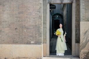 Graceful Vietnamese girl in green Ao Dai with yellow flowers at sacred pagoda-3
